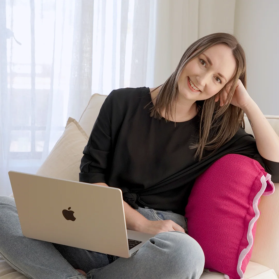 Photo of Kirstin McLachlan sitting on a couch, smiling with a MacBook Pro laptop on her lap.