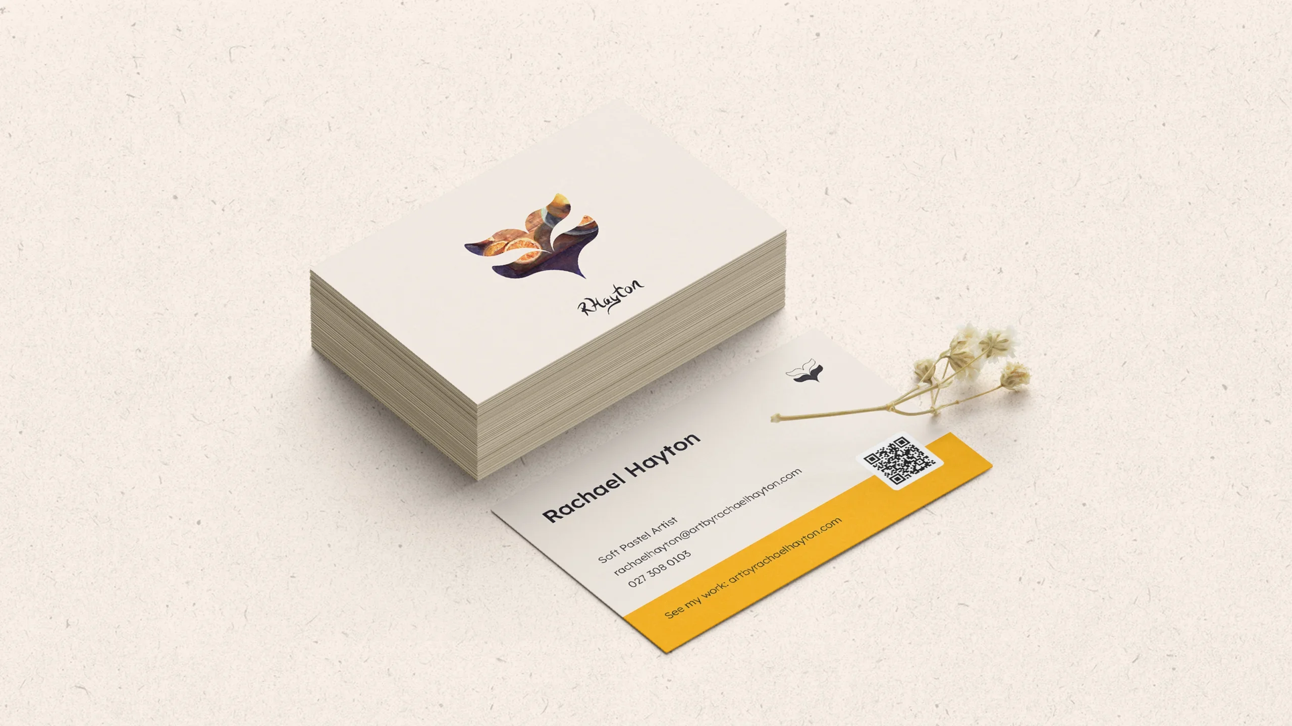 A stack of business cards with a whale tail icon and a yellow stripe decorated with a single dried flower on the right all placed on a cream coloured recycled paper background