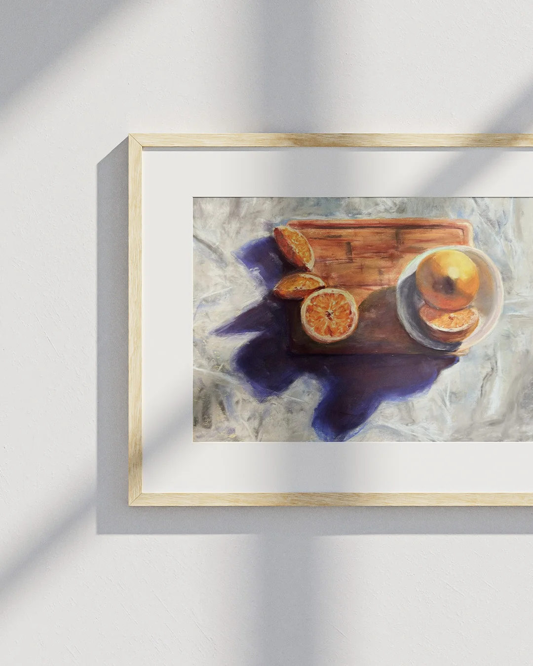 a pastel artwork depicting cut oranges on a wooden chopping board in a light wood frame